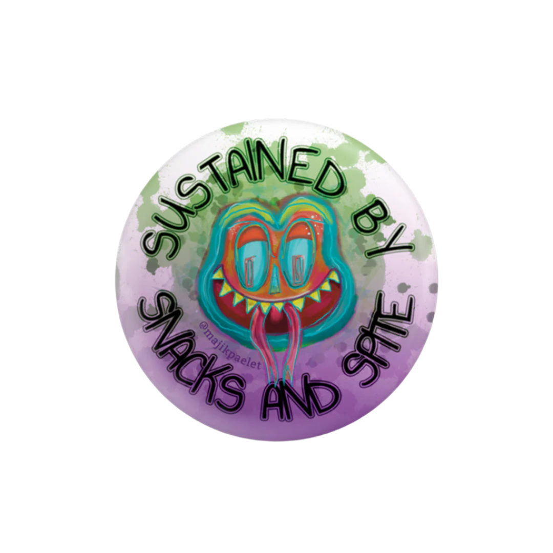 Brightly-colored frog-like original creature with it's tongue on a 2.25 inch round button that says "Sustained by Snacks and Spite" An original design by Majik Paelet (magic palette)
